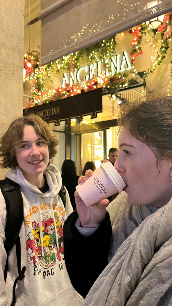 Teenage boy and girl drinking a warm drink in front of a store called Angelina in Paris