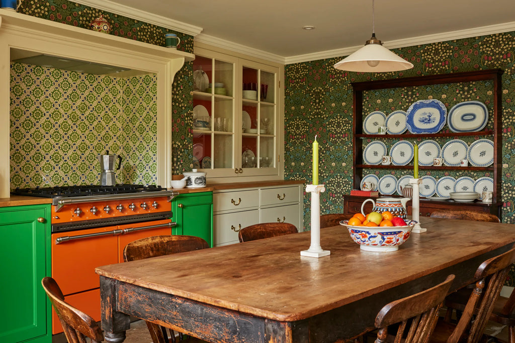 Charming old kitchen, with patterned green wallpaper and large, worn wooden table in the center