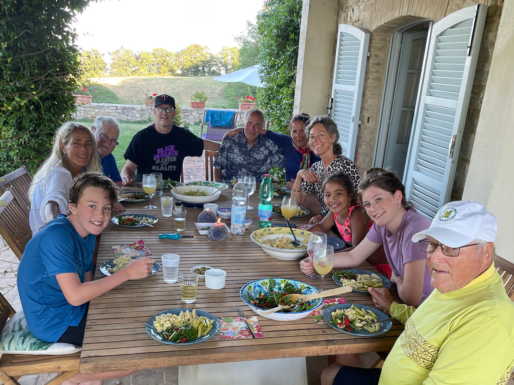 Family gathered around a big wooden table eating dinner outdoors