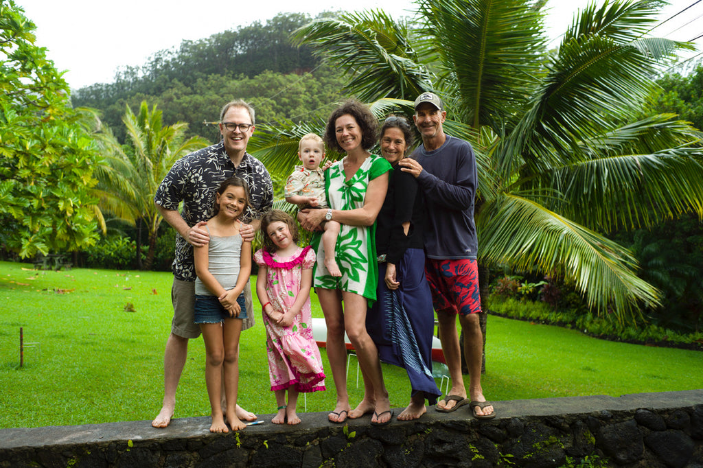 Two women, two men, and three kids hanging out in Hawaii in front of a lush backyard