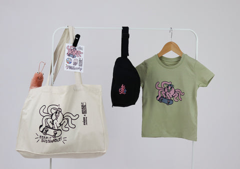 A t-shirt, tote bag, and purse hanging on a white rail on a grey background