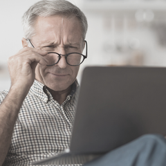 Man struggling to see laptop screen, holding glasses off face and squinting.