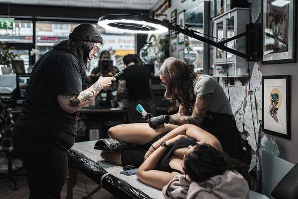 Sophie taking a photo of Amanda tattooing her customer