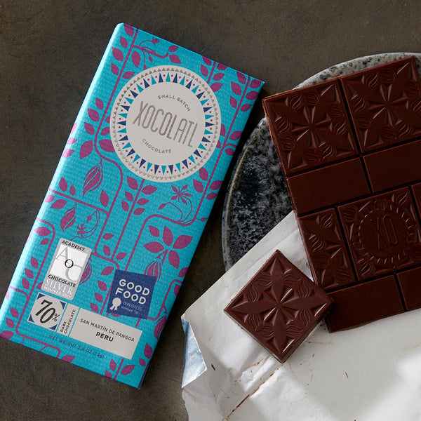 Pretty unwrapped chocolate bar lying beside Xocolatl's Peru 70% single-origin bar in a light blue and purple wrapper.