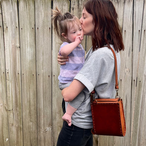 Jen Lewis of Purse & Clutch holding her child while wearing the ethical, sustainable Ellie Handbag | Wearwell