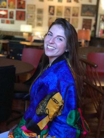 A smiling woman in a blue jacket is turned sideways. Her face is turned forward.