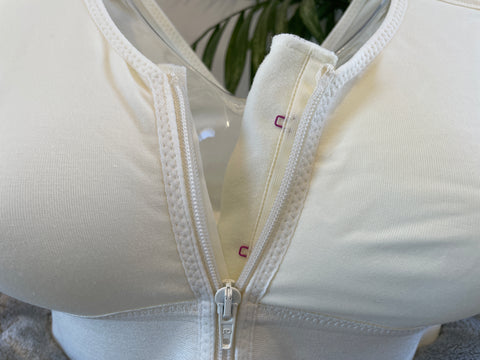 Close up picture of our post-surgery bra, Cara, showcasing the zip. The Cara bra includes a zip and adjustable straps to help with recovery. Cara is a white compression bra designed for comfort and support following surgery.