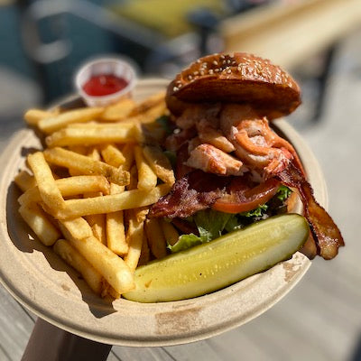 Lobster BLT, fries, and a pickle on a white plate