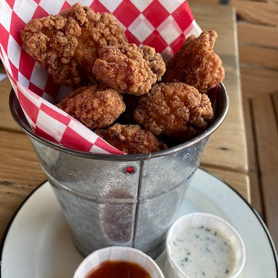 Fried popcorn chicken in a basket lined with wax paper next to a plate with sides of honey mustard and ranch