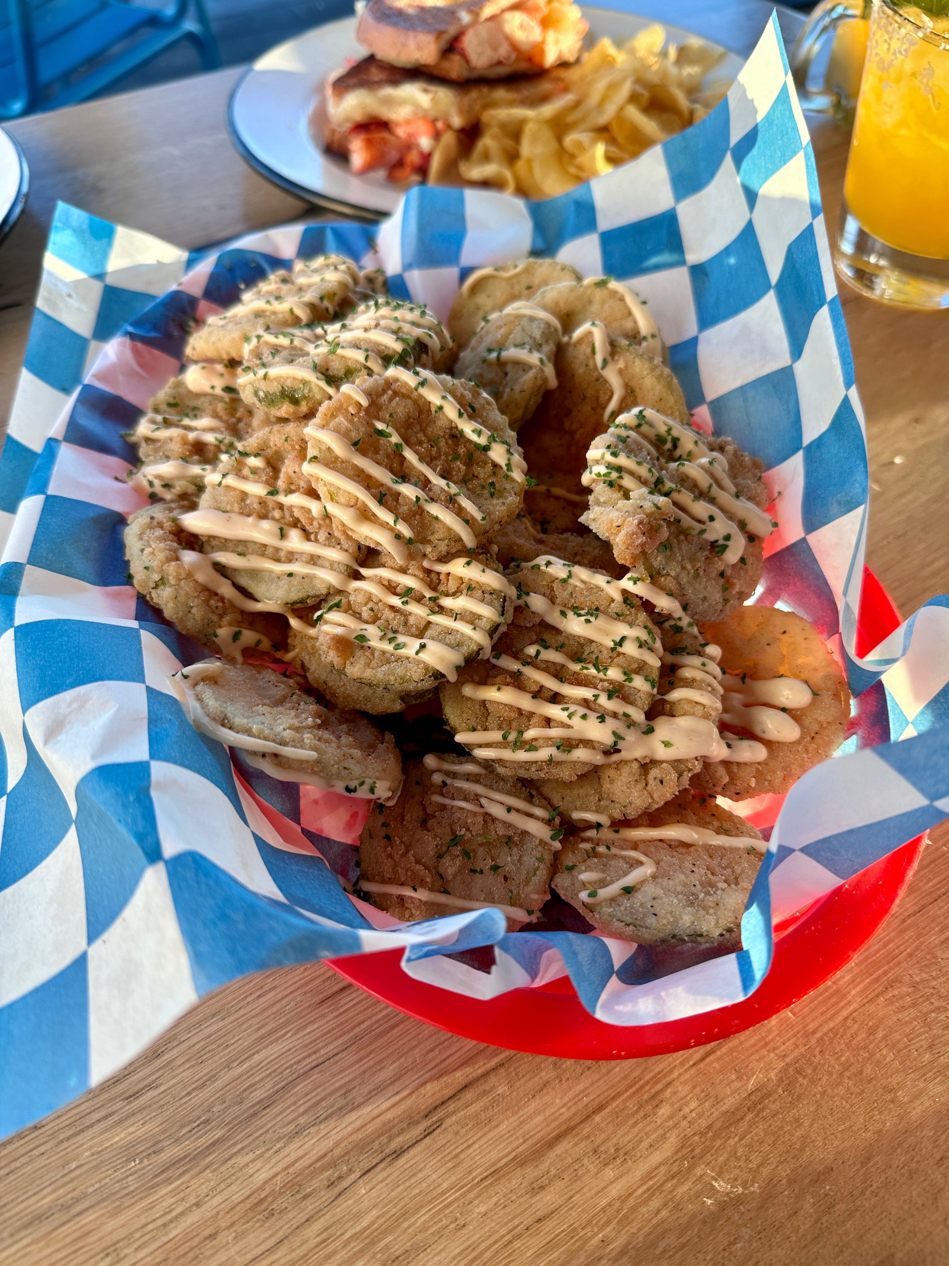 Fried pickles with drizzled spicy aioli in a basket lined with wax paper