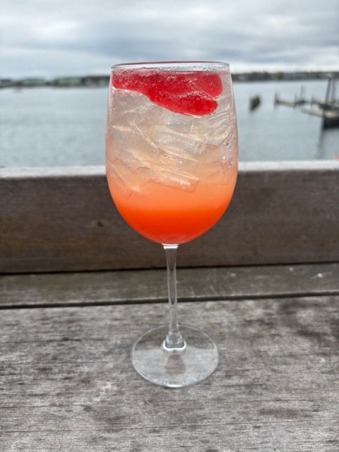 a wine glass with a pink cocktail with strawberries on the deck in front of the ocean