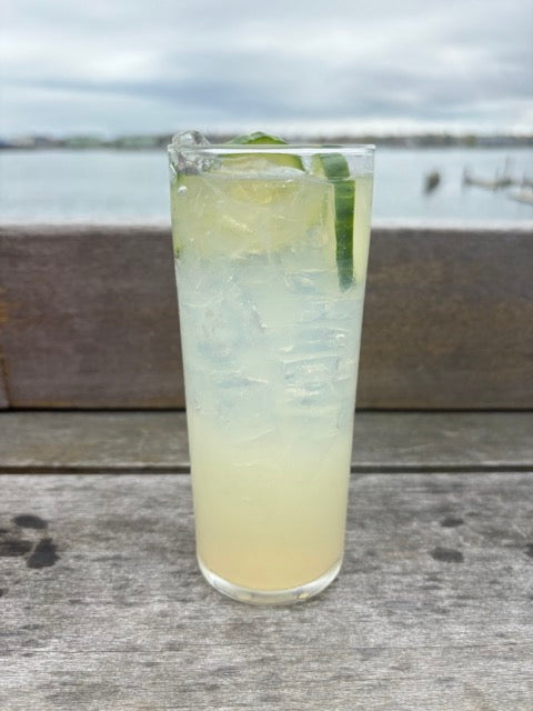 a yellow cocktail with cucumbers on the deck in front of the ocean
