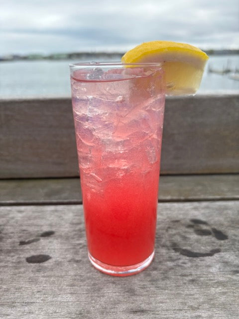 a pink cocktail on the deck in front of the ocean