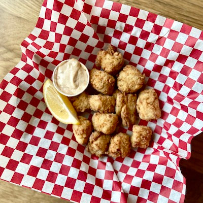 Fried haddock bites and tartar sauce in a basket lines with red and white wax paper