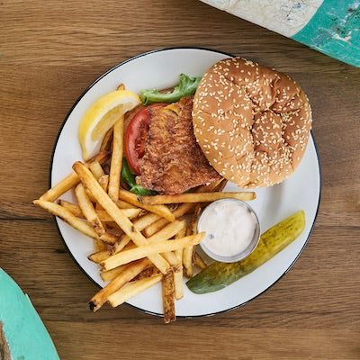 A haddock sandwich, fries, pickle, and a lemon on a white plate
