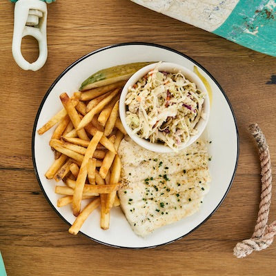 Broiled haddock, fries, lemon, tartar sauce, and a pickle on a white plate