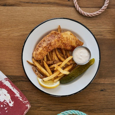 Fried haddock, fries, lemon, tartar sauce, and a pickle on a white plate