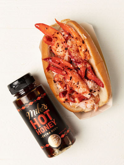 Luke's Spicy Honey Butter Lobster Roll and a bottle of Mike's Hot Honey on a white table