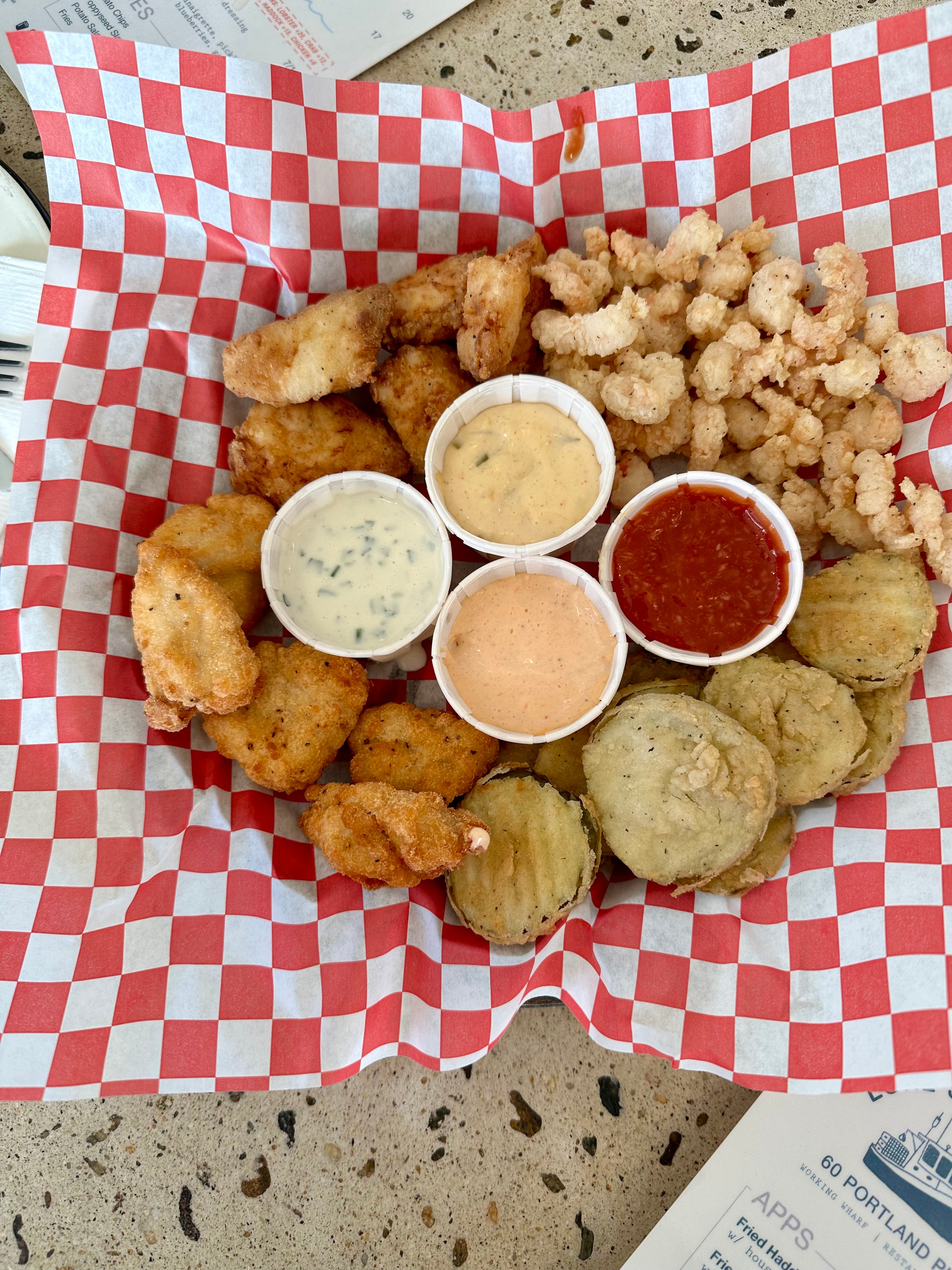 haddock bites, fried shrimp, popcorn chicken, fried pickles and various sauces in a basket lined with wax paper