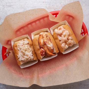 Halved lobster, crab, and shrimp rolls in a red basket lined with wax paper