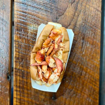 A warm lobster roll in a white paper sleeve on a wooden table