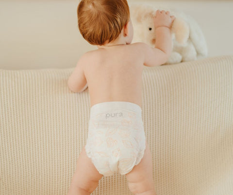 Baby reaching for a teddy in a Pura eco nappy