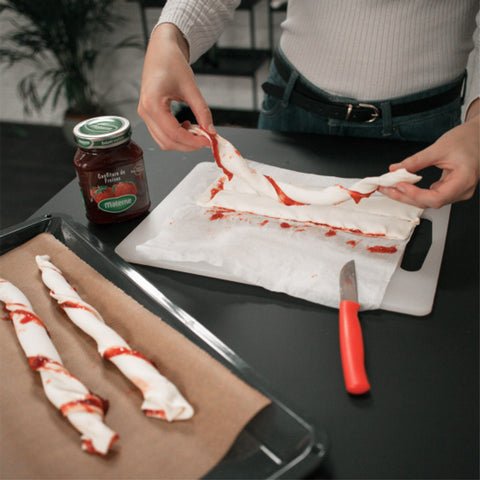 Avec un couteau aiguisé, coupez la pâte en fines bandes. N'appuyez pas trop pour éviter que la confiture ne coule sur les bords. Prenez une bande, tenez-là aux deux extrémités et tournez pour créer une torsade. Faites la même chose avec toutes les bandes.