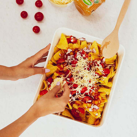 Recouvrez les nachos de sauce aigre-douce. Ajoutez les dés de tomate et l’oignon rouge, puis une couche de fromage râpé.