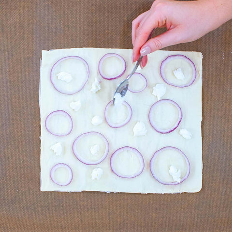 Rol het bladerdeeg met bakpapier uit op de bakplaat en bedek het met de rode ui in ringen en stukjes geitenkaas.