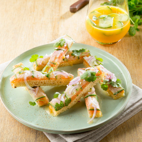 Meng alle ingrediënten voor de vinaigrette? Marineerer de zalm in gedurende 20 minuten. Schik de zalm op de toast met daarop flinterdunnesneetjes komkommer en rode ajuin. Snijd de toast in 4 gelijke repen. Presentatie : Schik de reepjes toast en werk af metkorianderblaadjes, witte peper en druppels vinaigrette. Serveer met de cocktail afgewerkt met komkommer enkoriander.