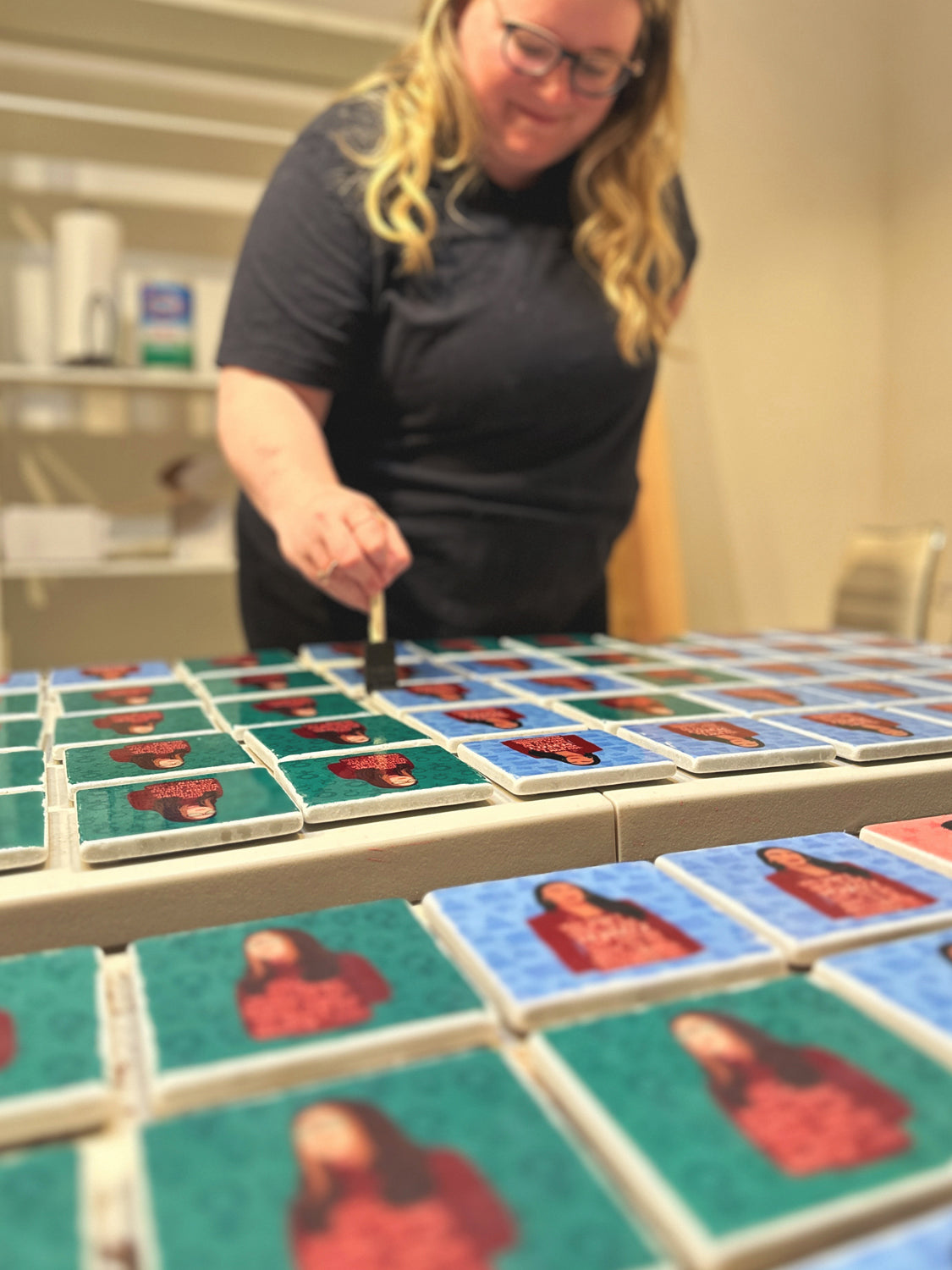 woman brushing gloss gel on marble coasters on a table in a workshop