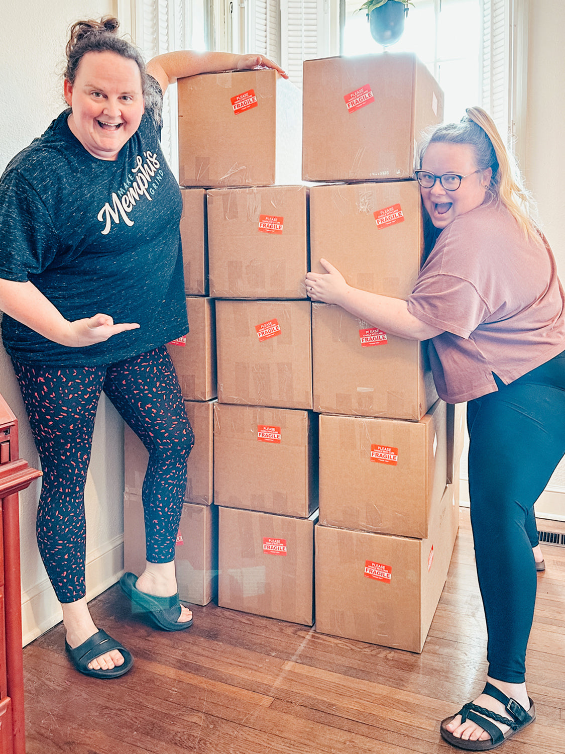 two women standing on both sides of a stack of brown shipping boxes