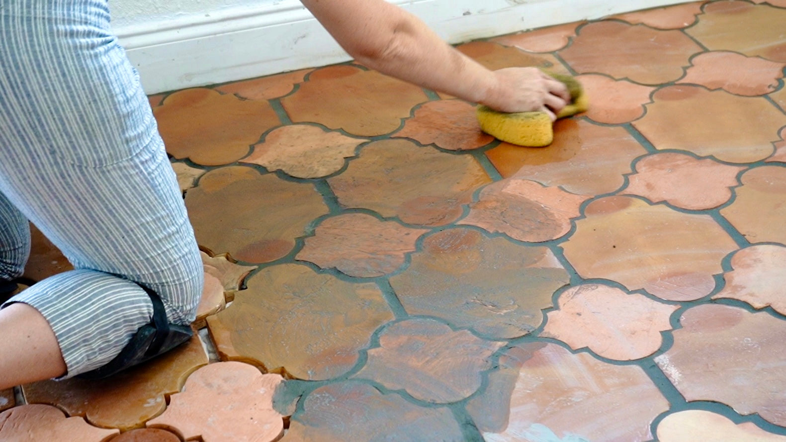 Person on knees scrubbing terracotta shaped tile floor clay imports