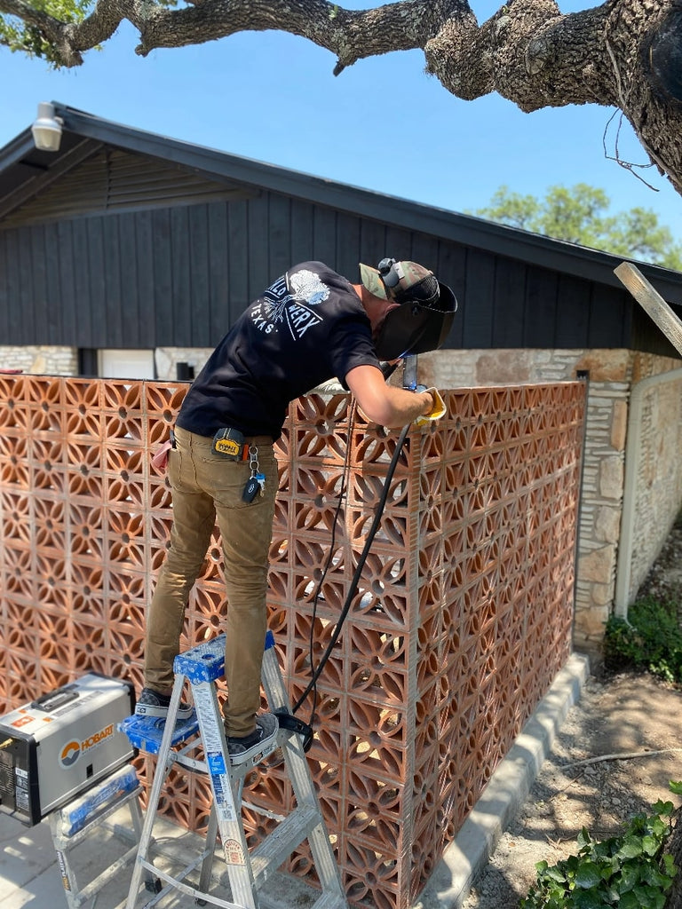 Man welding breeze block wall frame outside of home