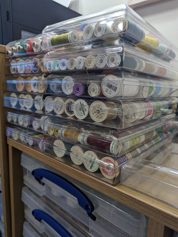 Many Fererro Rocher chocolates boxes, full of reels of coloured thread, stacked up on a shelf.