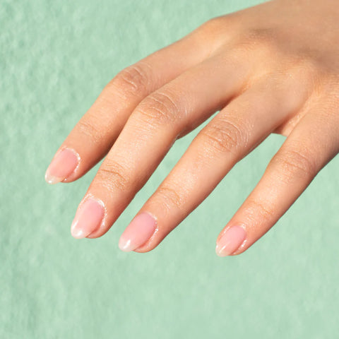 A model's hand painted with sheer honey beige Hello Birdie classic polish on a pistachio green stucco background