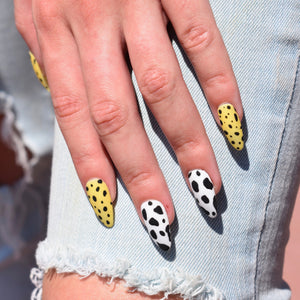 Hand-painted gel polish nail art press-ons in an almond shape.  A modern take on animal print nail art with the thumb, index finger and pinky in a yellow backed animal print and the middle and ring finger in a white backed print.  All nails have a matte finish.  One had is pictured over a pale denim jeans with distressed holes a the knees.   