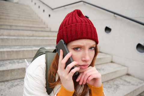 woman on phone looking worried sitting on staircase outside