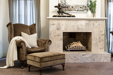 A marble fireplace with a chair next to it with a rug and pillow