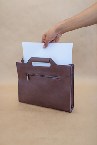 hand putting paper in a brown leather bag