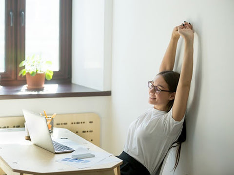 woman stretching arms at desk at home while working