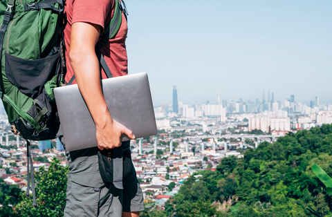 man holding laptop while looking over the city with backpack