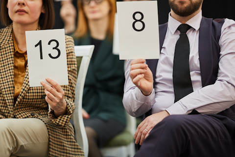 A man and women at an auction holding up a sign for an 8 and 13
