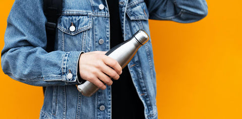 A person wearing a denim jacket and holding his Travah water bottle diversion safe