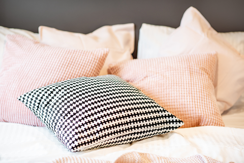 Some pink and white and some black and white pillows on a bed.