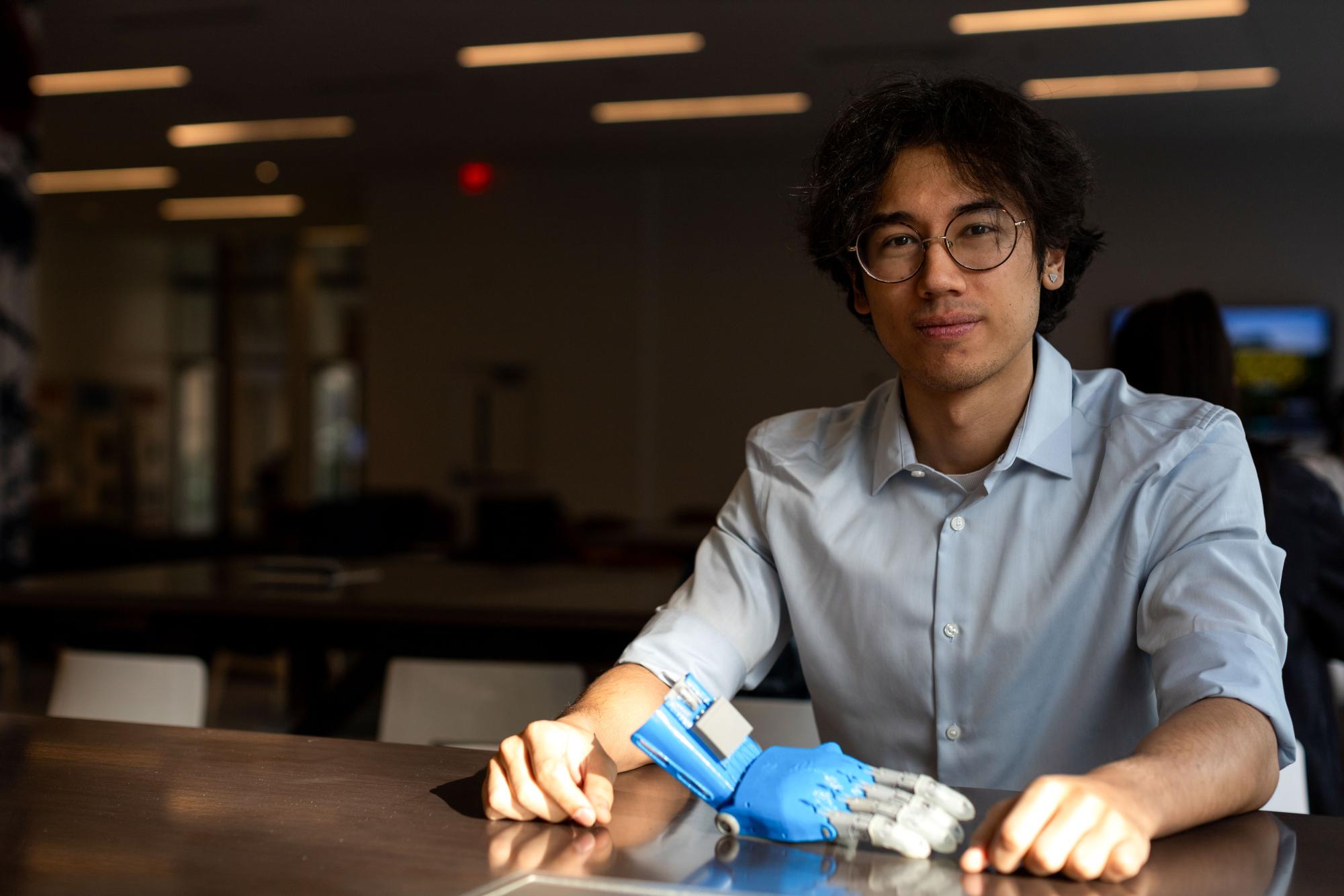 Senior Alec Tripi, a member of the GW Biomedical Engineering Society, sits with a prosthetic hand that his team has produced.