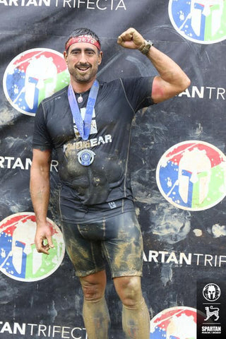 Spartan Trifecta athlete Nick Klingensmith flexes with his medal and MudGear after a grueling race.