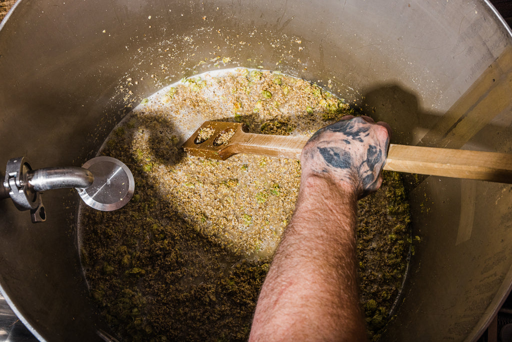 Brewer making beer by stirring whole cone hops into the mash process.