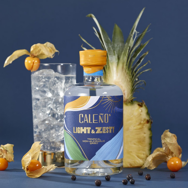 Navy blue background featuring a glass of Caleno alcohol free spirit and a pineapple cut in half. In the front is a bottle of Caleno's Lighty and Zesty alcohol free spirit.