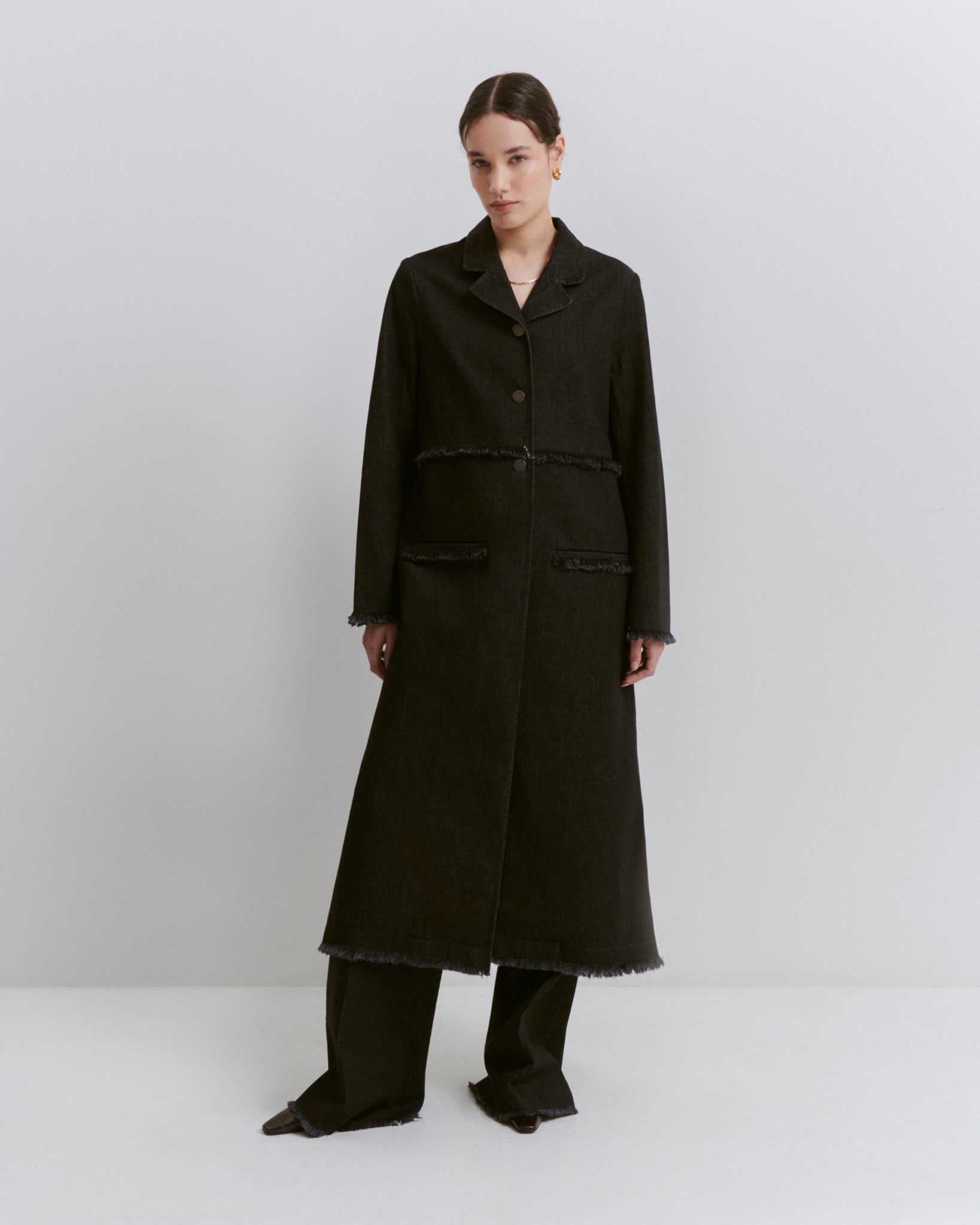 model wears Issue Twelve black denim coat in organic cotton with organic cotton black trousers